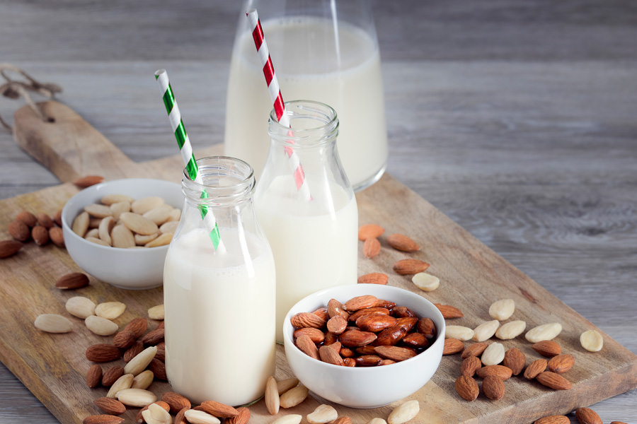Receta de cóctel de almendras sin alcohol Imagen de ambiente "cóctel de almendras sin alcohol": dos botellas de cuello ancho llenas con pajitas de colores sobre una tabla de madera con almendras.