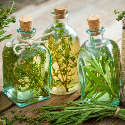 Tres botellas de vidrio transparente llenas de aceite aromatizado, cerradas con un corcho.