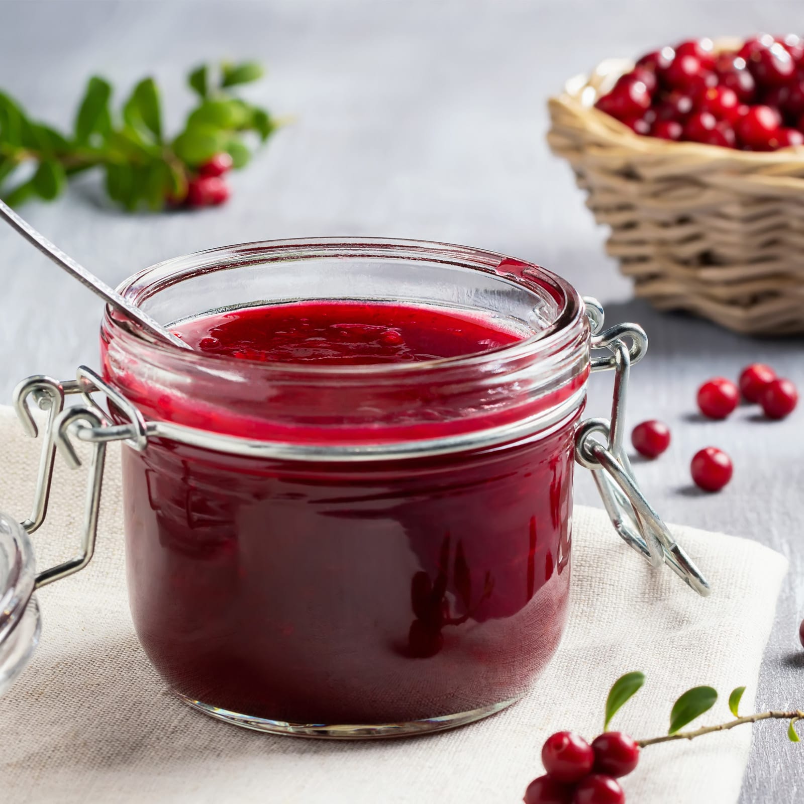 Pequeño frasco de alambre lleno de mermelada casera roja, dispuesta sobre una servilleta de tela con frutos rojos.